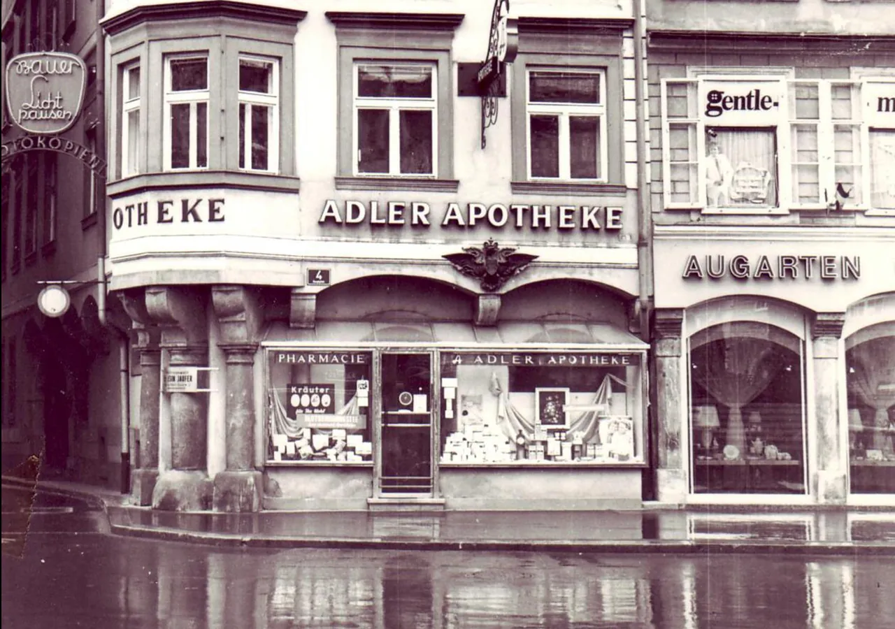 Historisches Foto der Adler Apotheke aus den 1950er-Jahren mit Schaufenster und regennasser Straße