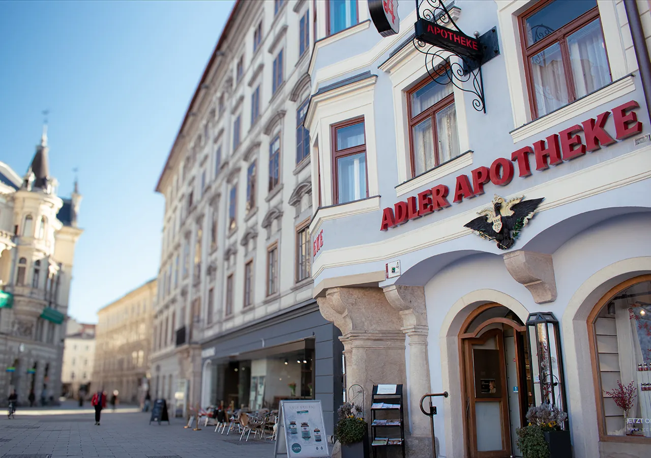 Fassade der Adler Apotheke mit Adler-Emblem und Schriftzug, im Hintergrund der Grazer Hauptplatz