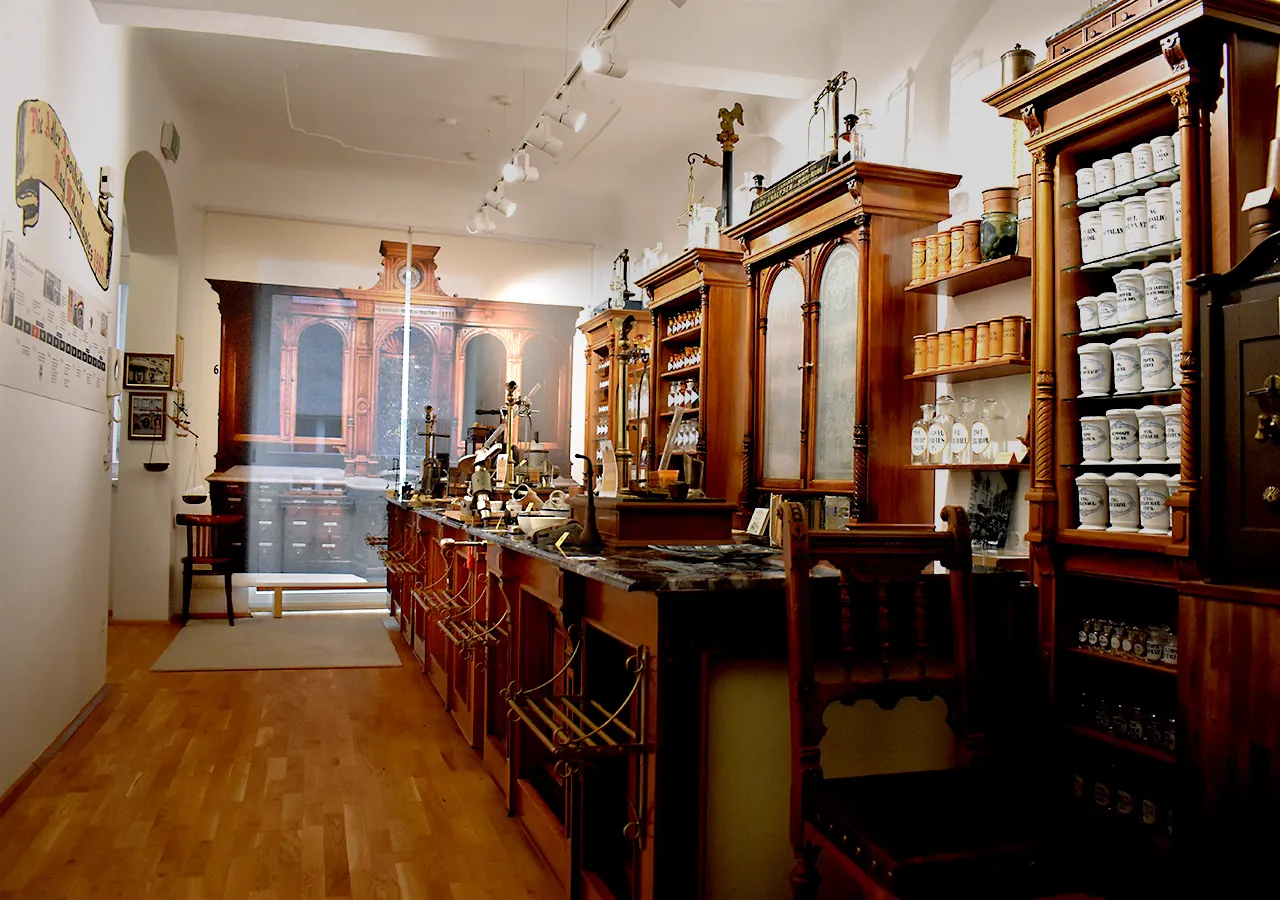 Hauptraum des Museums mit Holztischen voller Exponate und einem Zeitstrahl zur Geschichte der Apotheke