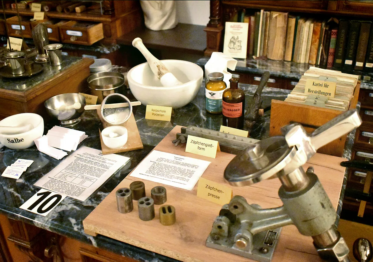 Schalen, Mörser und beschriftete Flaschen auf einem Marmortisch im Adler Apotheken Museum