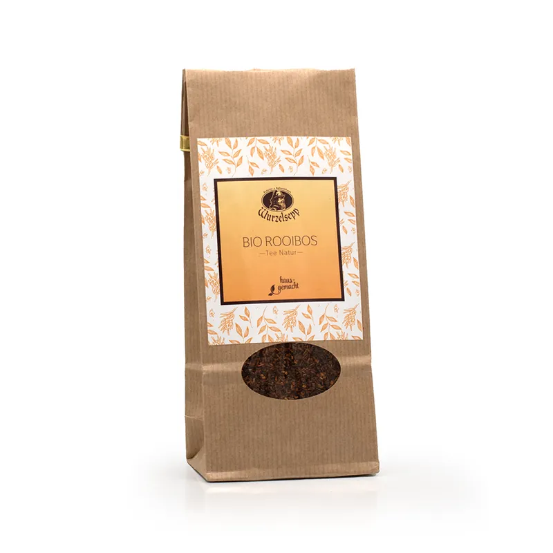 Ein Sackerl in hellbraun mit kleinem ovalen Sichtfenster und weißem Etikett mit feinen orangen Blättern, innen hell orange. Wurzelsepp Bio Rooibos Tee.
