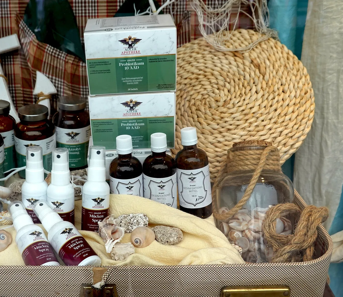 Schaufenster der Adler Apotheke mit Grazer Hausspezialitäten: Grazer Probiotikum, Mückenspray, Elektrolytlösung und Desinfektionsmittel